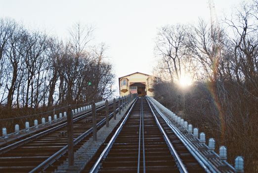 A scenic view of an inclined railway in Pittsburgh at sunset during wintertime, surrounded by leafless trees.