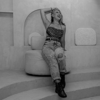 Stylish woman in casual attire laughing and seated in a contemporary indoor space.