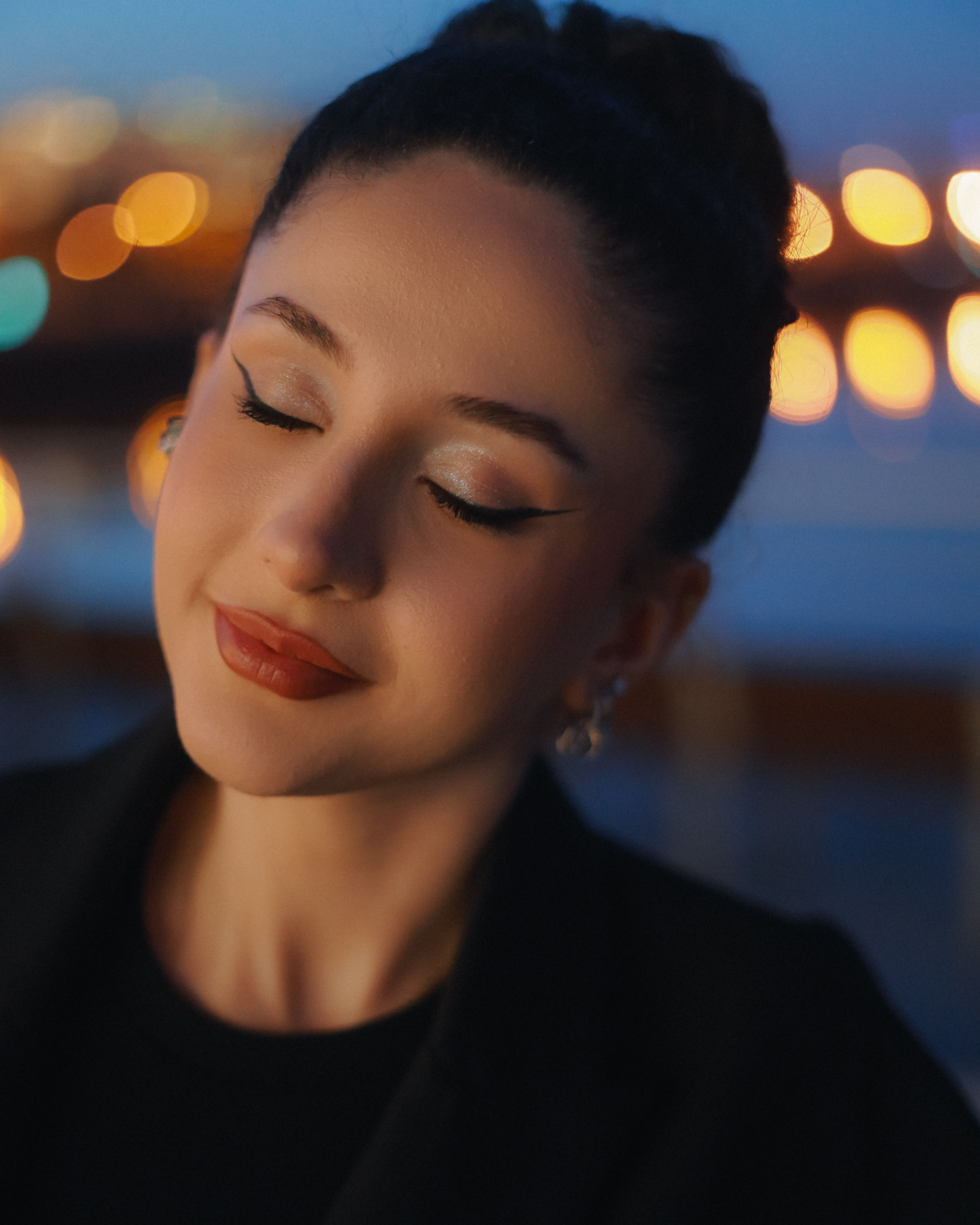 Portrait of a woman with closed eyes, surrounded by urban night lights and a serene mood.