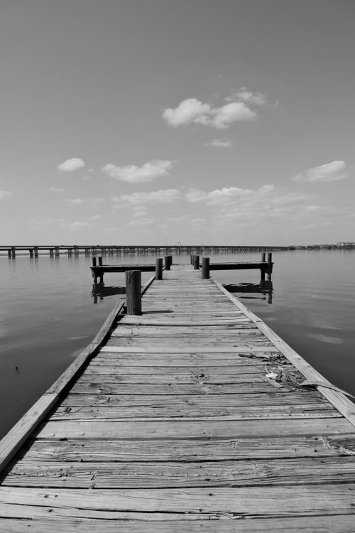 Free A serene wooden pier extending into a calm lake under a cloudy sky. Stock Photo