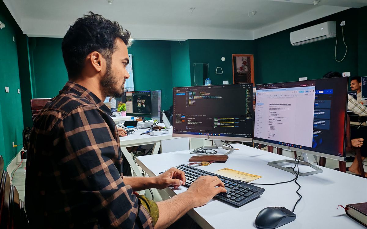 A software developer working on code at a dual monitor setup in a modern office.