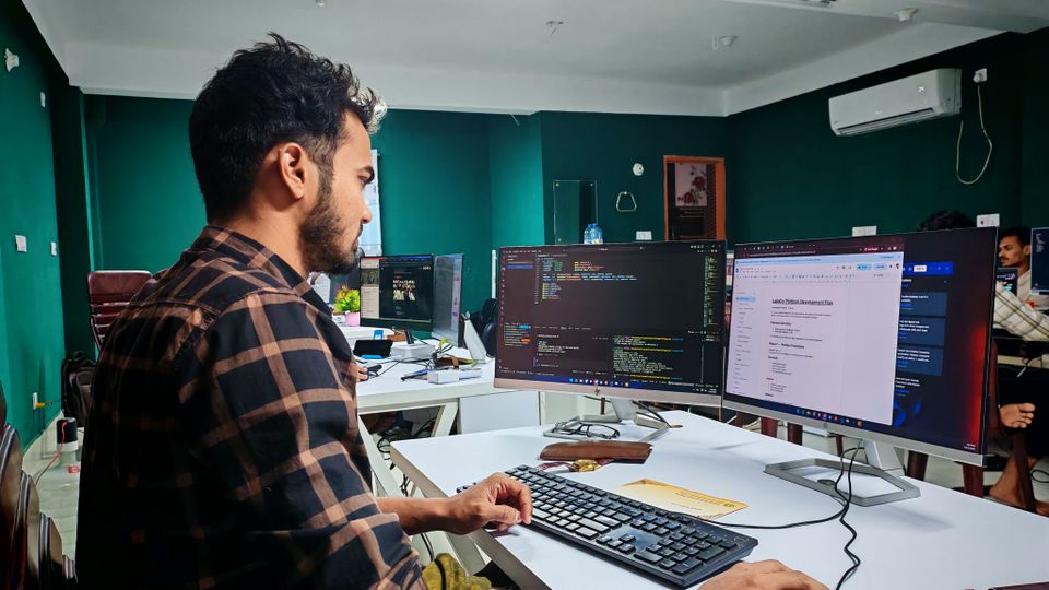 Pessoa desenvolvedora trabalhando com código em dois monitores em um escritório.
