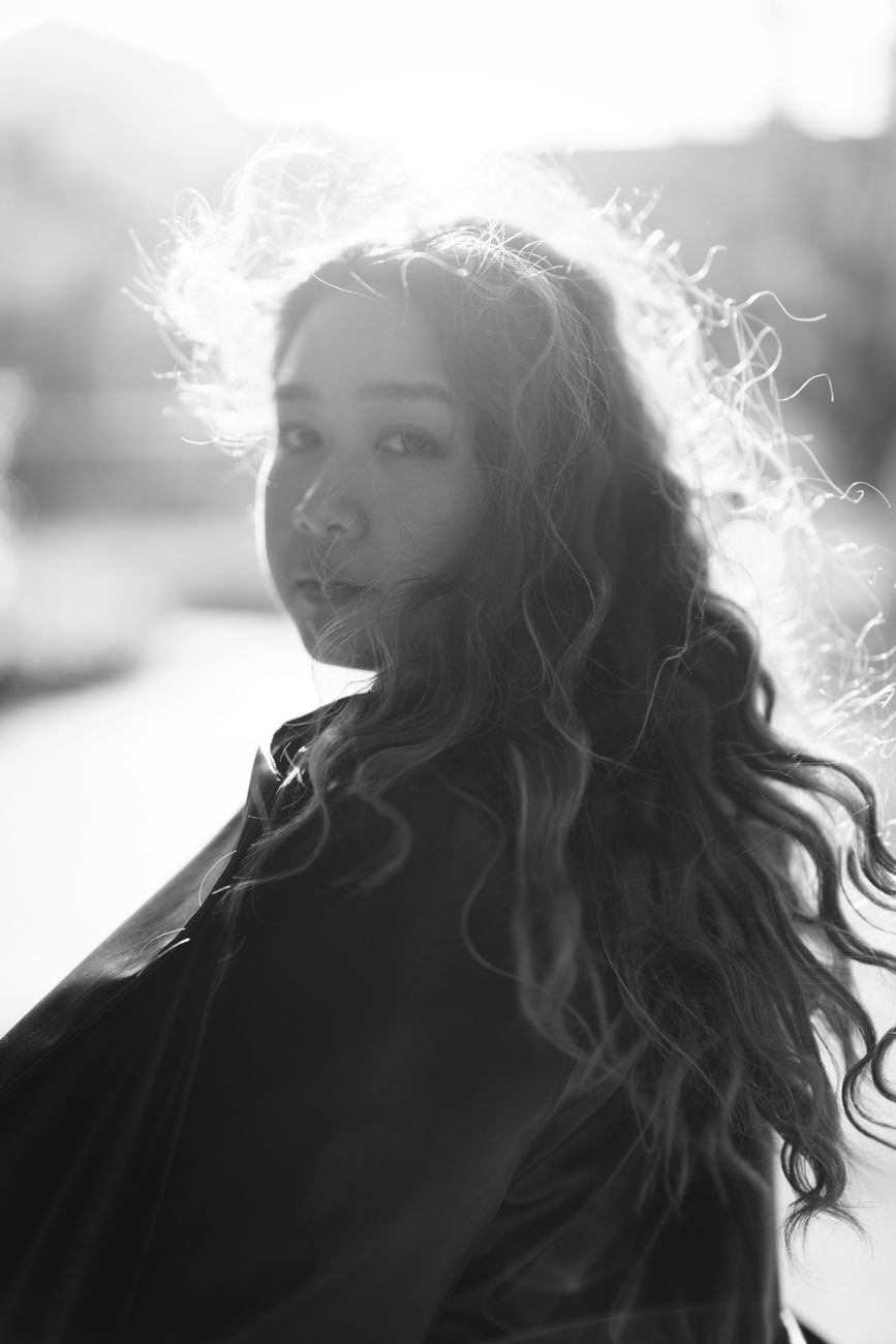 Artistic black and white portrait of a woman with curly hair in outdoor setting.