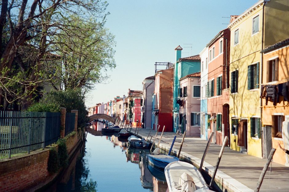 Vibrant buildings reflect in a serene canal in Burano, Italy.