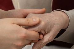 A younger person holds a senior adult's hand, symbolizing care and support.