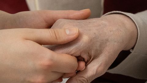 A younger person holds a senior adult's hand, symbolizing care and support.