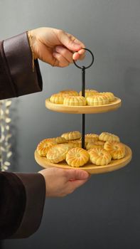 A hand presenting traditional mooncakes on a two-tier wooden stand, perfect for festive celebrations.