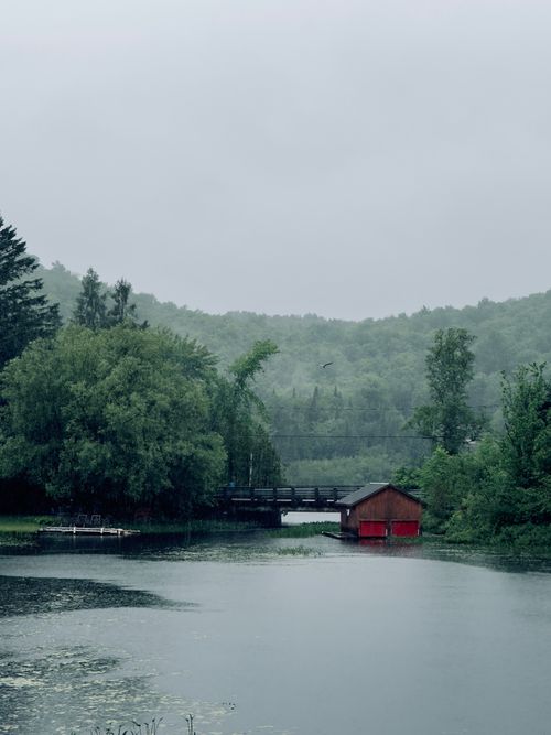 Free A red cabin by a tranquil lake surrounded by misty green forests, captured in Québec City, Canada. Stock Photo