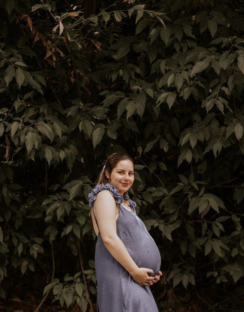 Free Pregnant woman in blue dress posing outdoors, surrounded by lush green foliage. Stock Photo