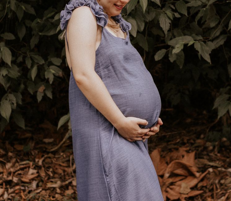 A woman in a blue dress enjoying nature during pregnancy, standing outdoors.