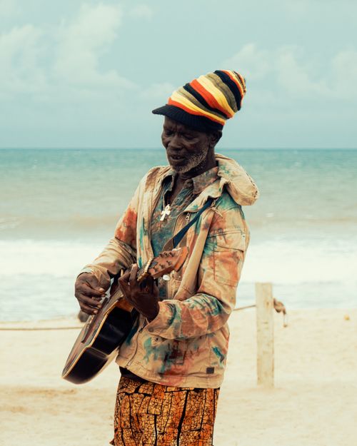 Free A joyful African musician playing guitar on a sunny beach, wearing colorful attire. Stock Photo
