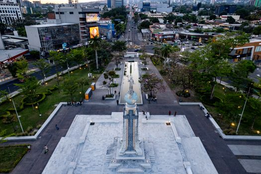 Aerial view of Monumento al Divino Salvador surrounded by cityscape of San Salvador, El Salvador at dusk.
