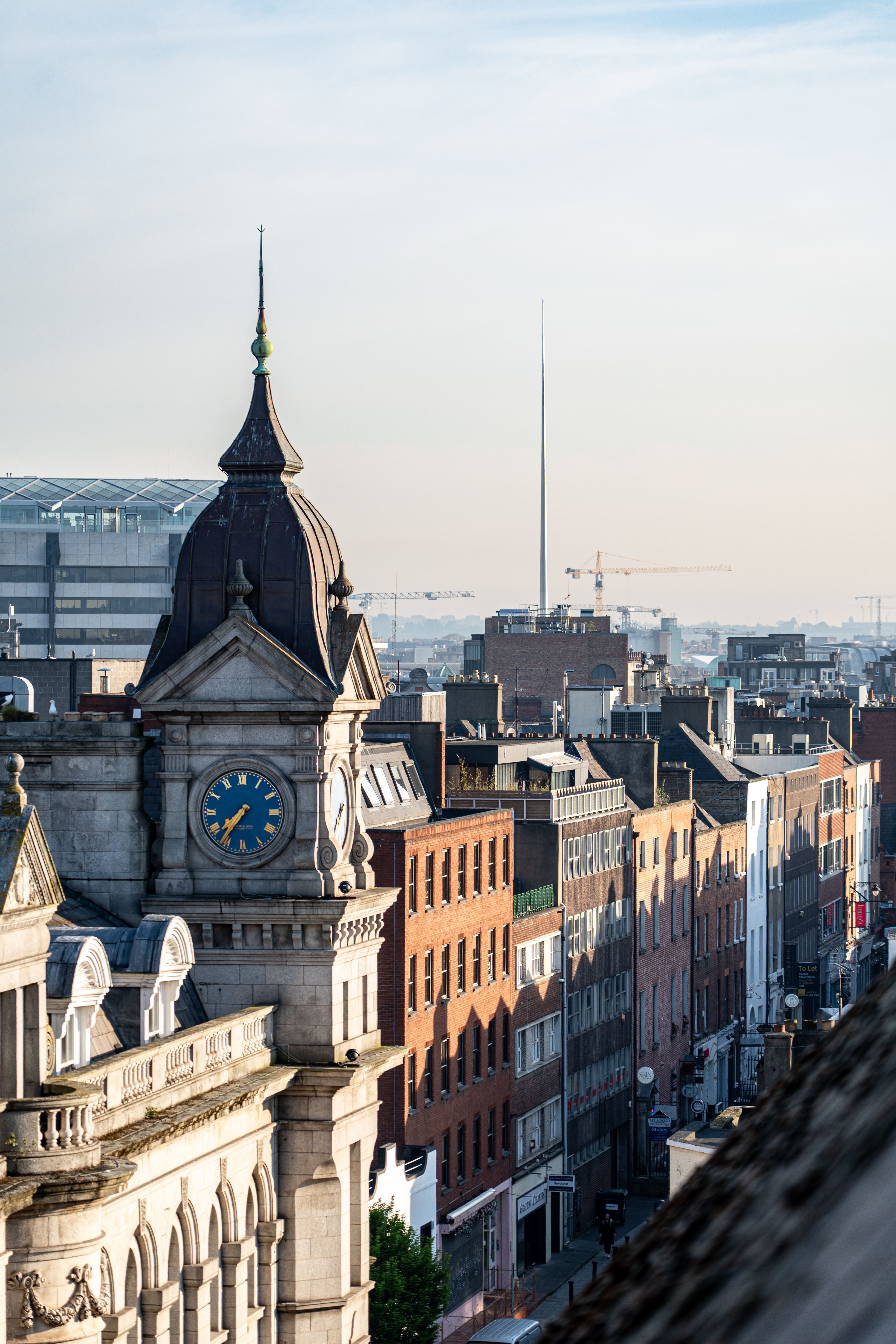 Scenic aerial shot of Dublin, Ireland cityscape with a historic clock tower in the foreground and The Spire visible at sunrise.