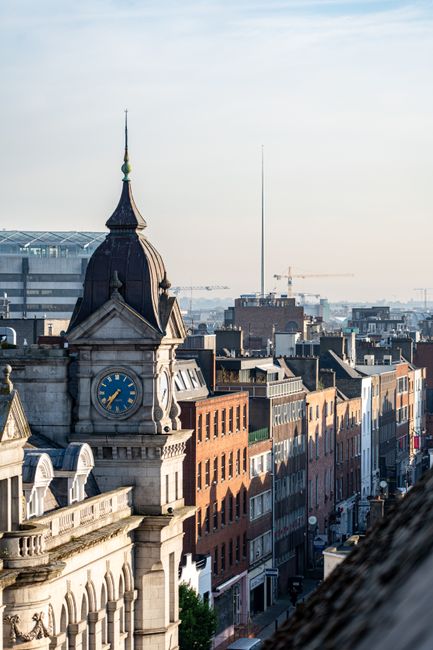 Scenic aerial shot of Dublin, Ireland cityscape with a historic clock tower in the foreground and The Spire visible at sunrise.
