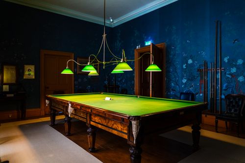 Free A sophisticated billiard room in Ireland with rich blue walls and a classic pool table under green lamps. Stock Photo