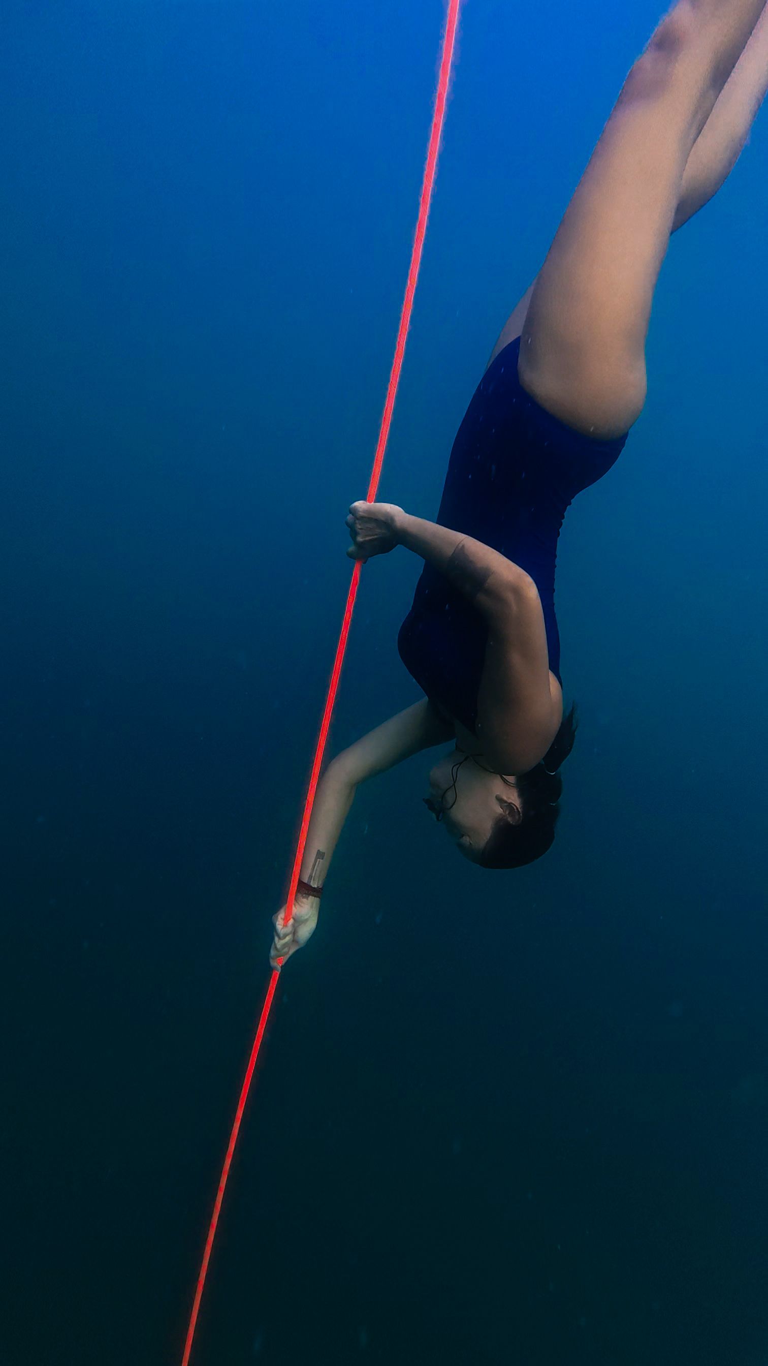 Fotomural Una buceadora en apnea desciende con gracia bajo el agua sujetando una cuerda roja, demostrando unas habilidades de buceo excepcionales.