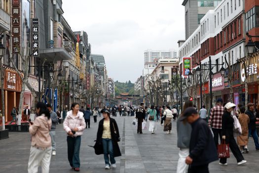 Crowded shopping street with people walking past shops and cafes in an Asian city center.