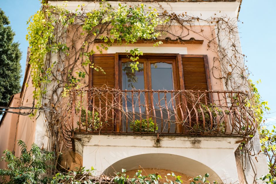 Beautiful Italian balcony with wooden shutters and lush vines in the sunlight, perfect for architectural inspiration.