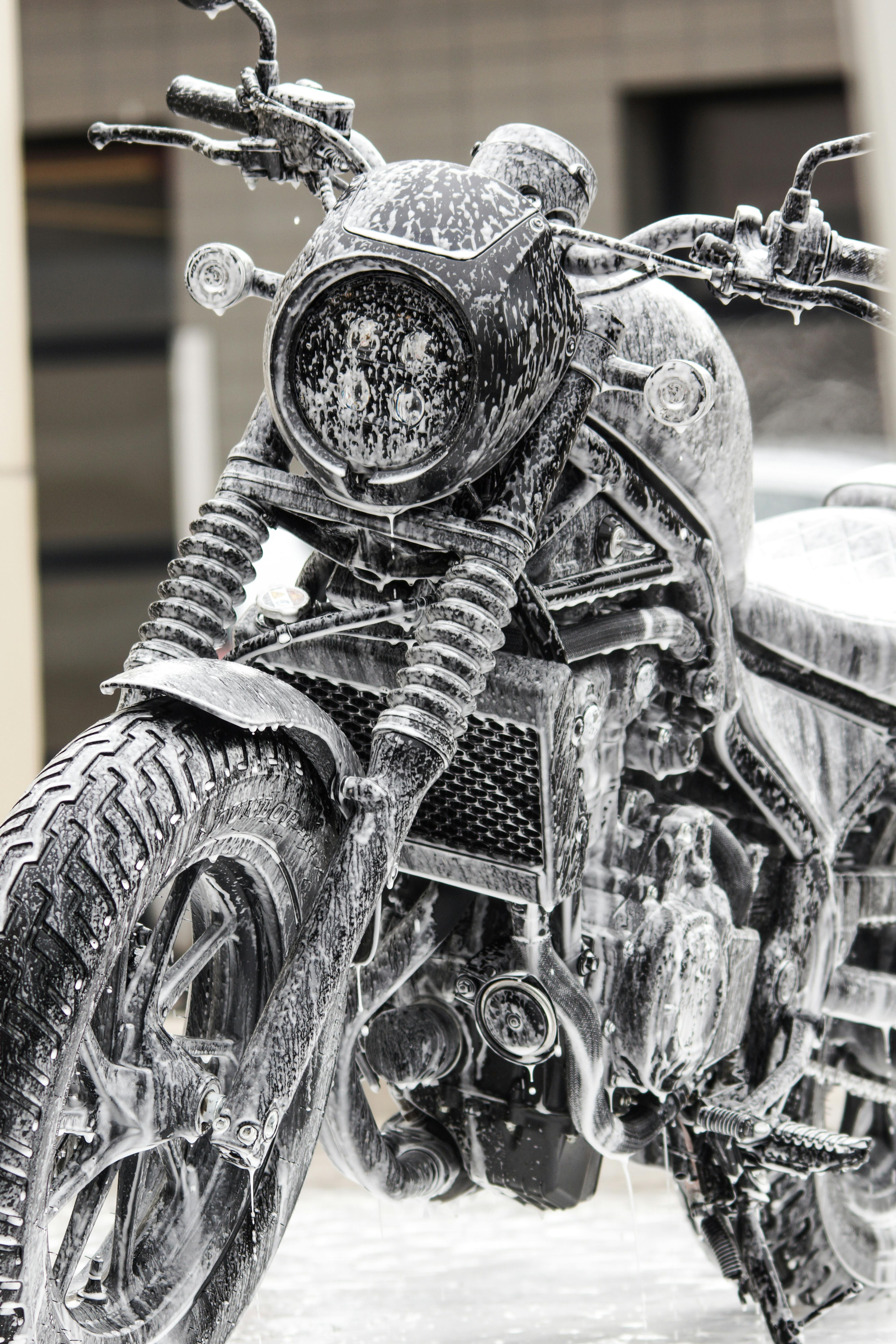 Detailed close-up of a motorcycle covered in foam during a wash outdoors.