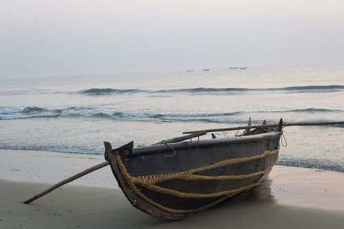 Free A rustic fishing boat rests on a serene beach at sunrise, with calm waves in the background. Stock Photo