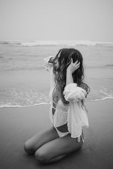 Stylish woman in swimwear kneeling on the beach, captured in a dramatic black and white photo.