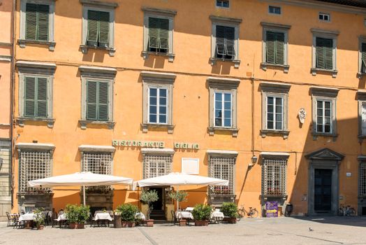 Sunlit historic building and outdoor cafe in Lucca, showcasing Tuscany's charming architecture.