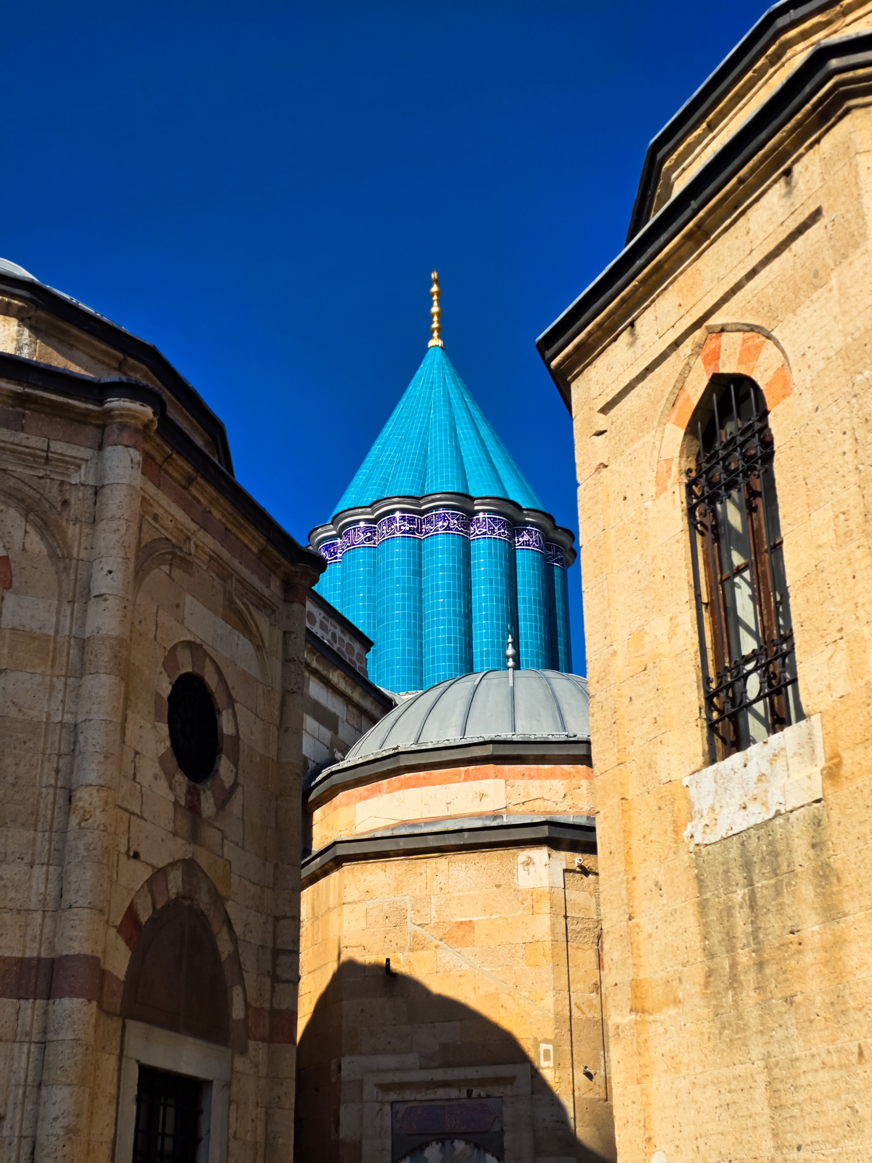 Vibrant blue dome of the Mevlana Museum surrounded by historic architecture in Konya, Türkiye.