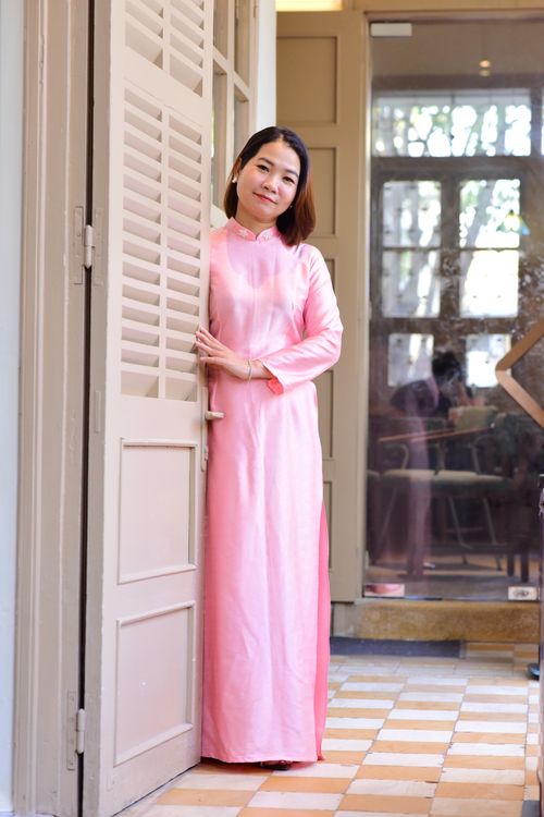 Free Asian woman smiling in a traditional pink dress standing by an open door indoors. Stock Photo