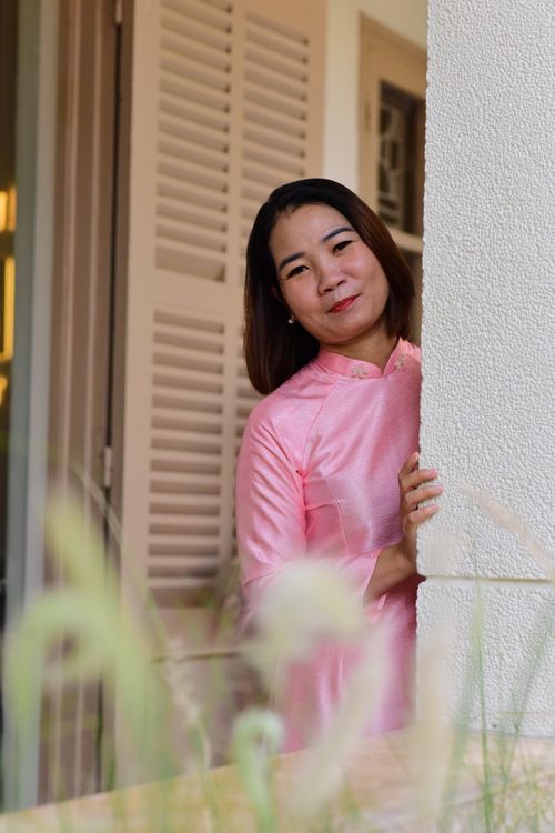 Free Woman in a traditional pink dress smiling while peeking around a corner outdoors. Stock Photo