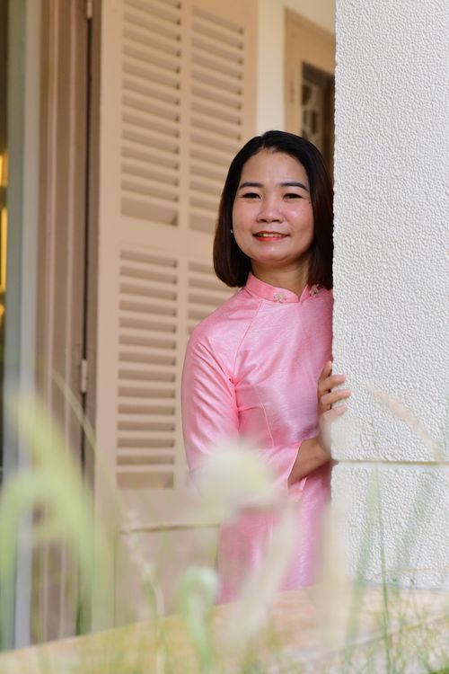 Free A young woman in a pink traditional dress smiles while standing indoors, creating a warm and inviting atmosphere. Stock Photo
