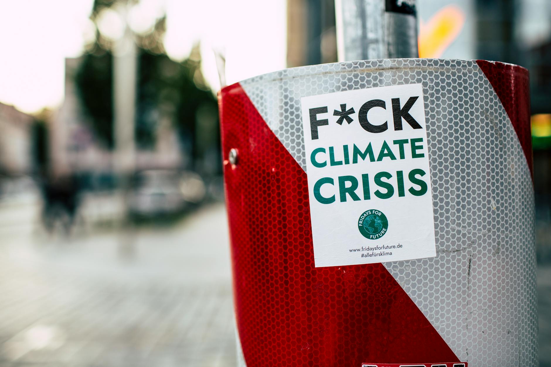 Sticker advocating against climate crisis on a red post in a city street, emphasizing climate action.