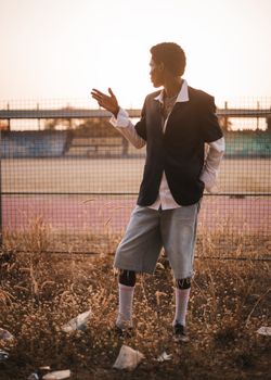 Man in casual outfit poses outdoors with a moody sunset backdrop.