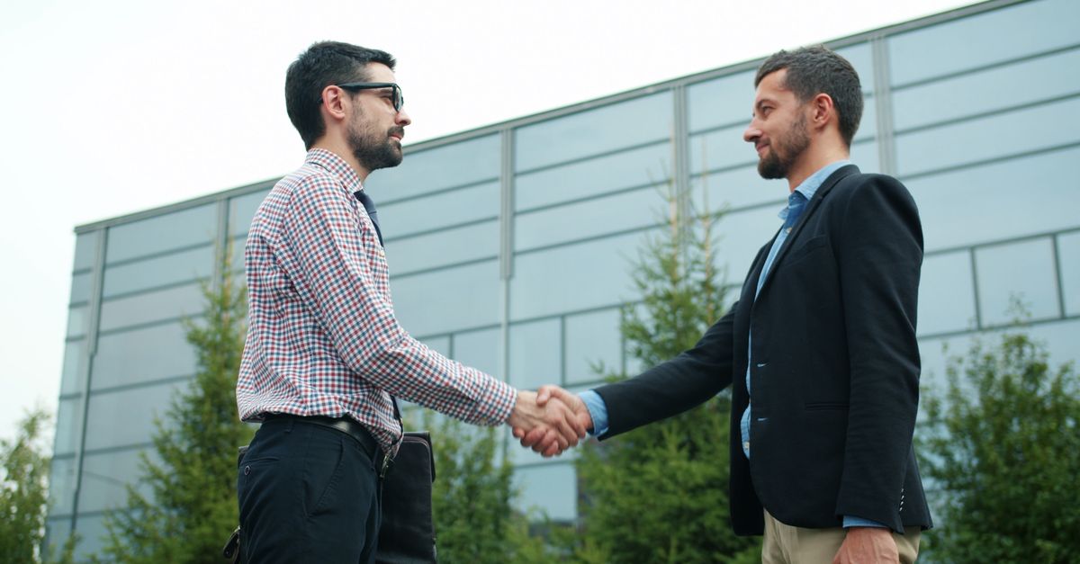 Dos empresarios estrechando la mano frente a un edificio de oficinas moderno, sellando una alianza estratégica para la digitalización de pymes.