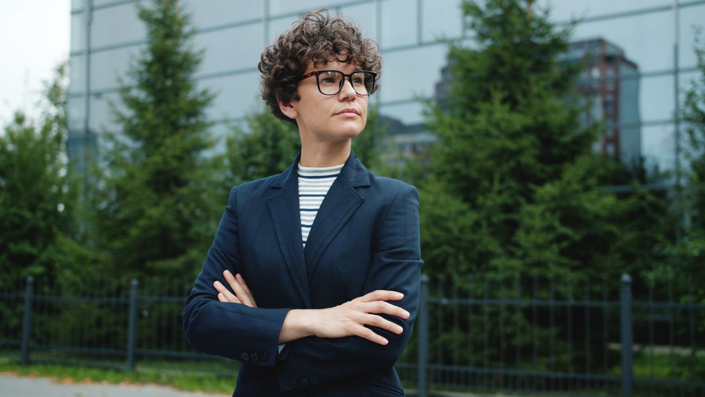 Confident woman in a suit with arms crossed, posing outside a modern building.