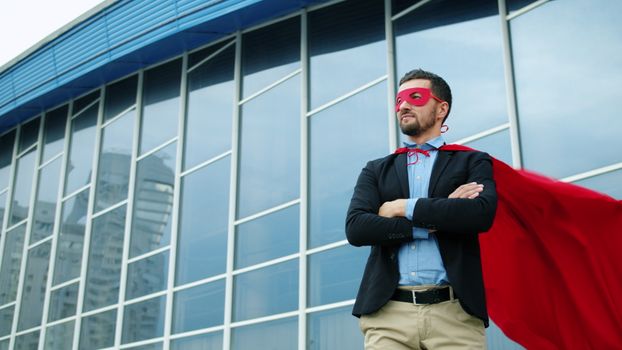 Businessman wearing a red cape and mask, standing confidently outside a modern building.