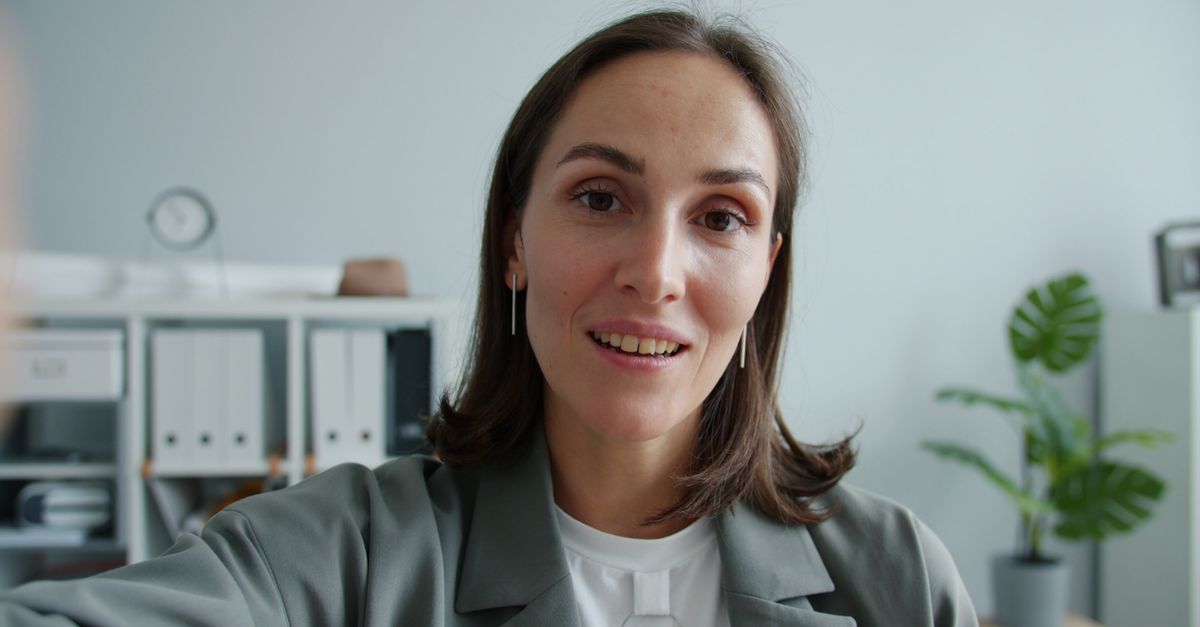 Close-up of a confident woman in an office environment, smiling at the camera.