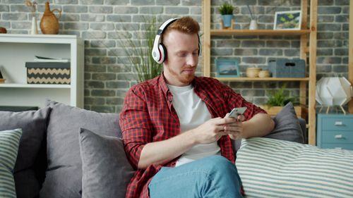 Free Man wearing headphones using smartphone on sofa, modern interior. Stock Photo