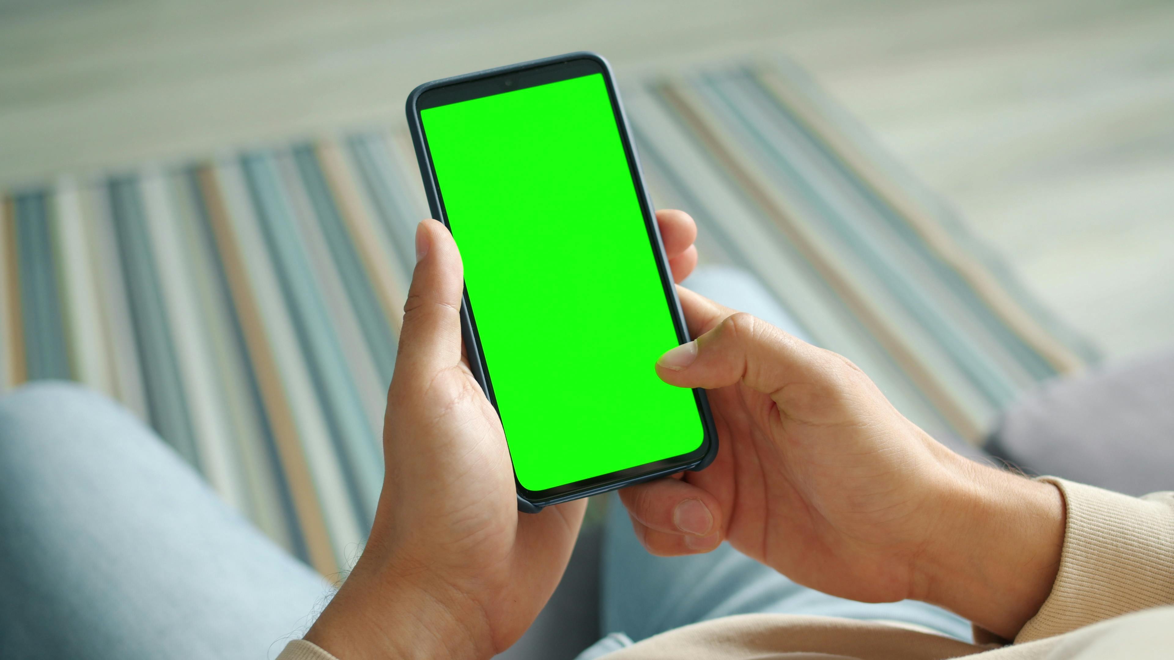 Hands holding a smartphone with a green screen, ready for customization.
