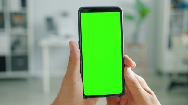 Close-up of hands holding a smartphone with a green screen, ideal for customization.