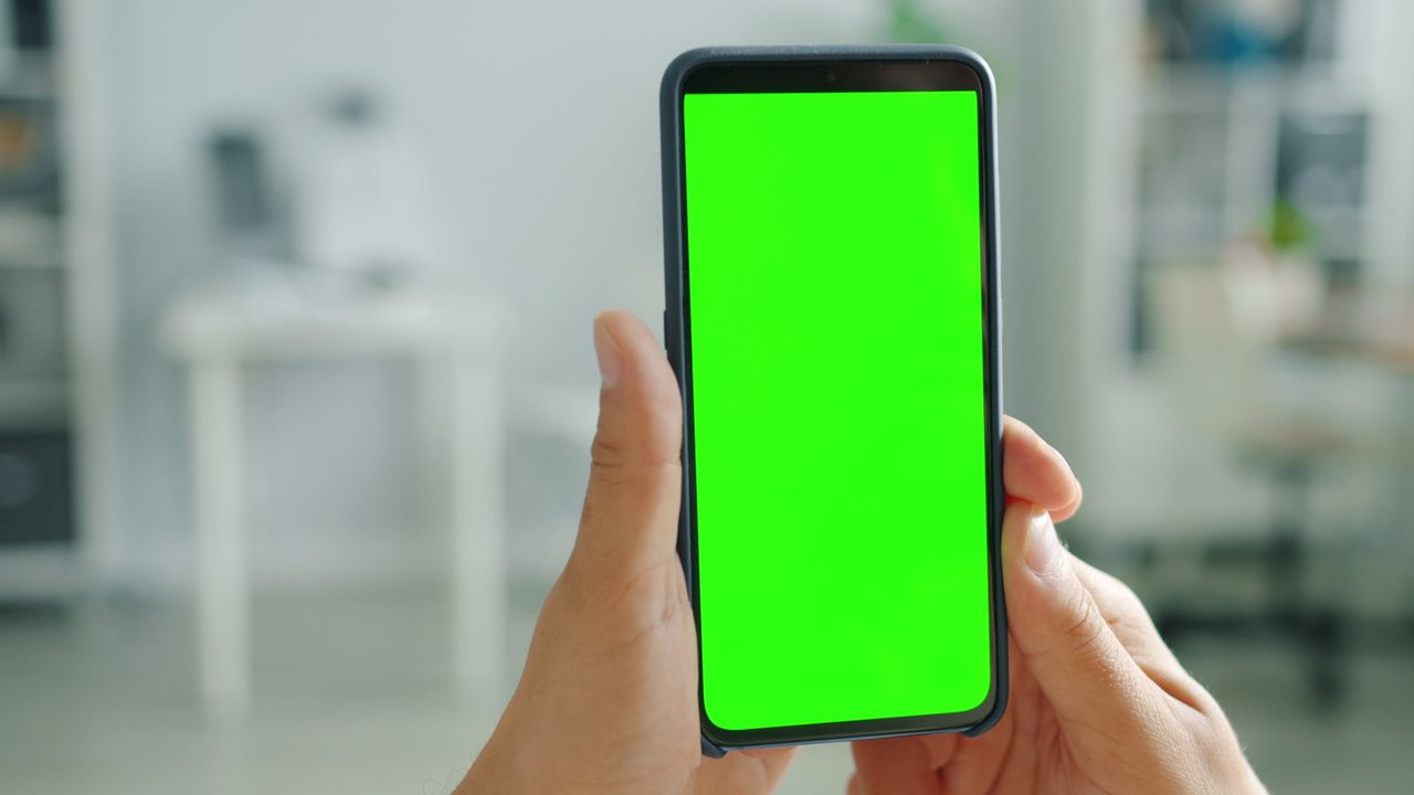 hands holding smartphone with green screen for mockup indoors