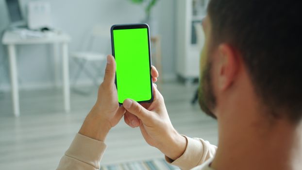 Man holding smartphone with green screen for mockup application indoors.