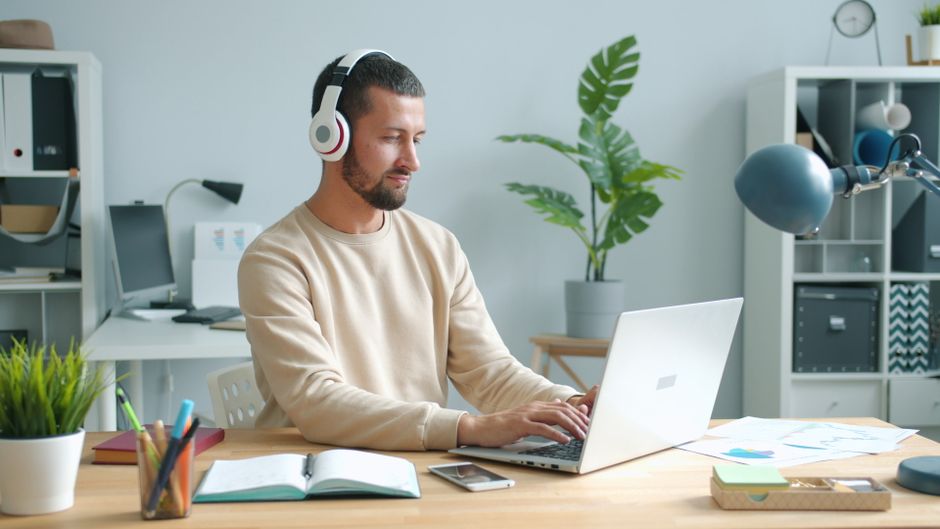 Adult man with headphones working on laptop in home office setting. Adult man with headphones working on laptop in home office setting.
