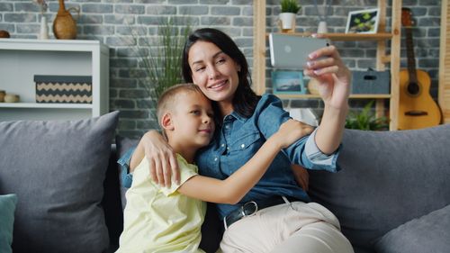 Free Mother and son happily taking a selfie on the couch, embracing family moments. Stock Photo