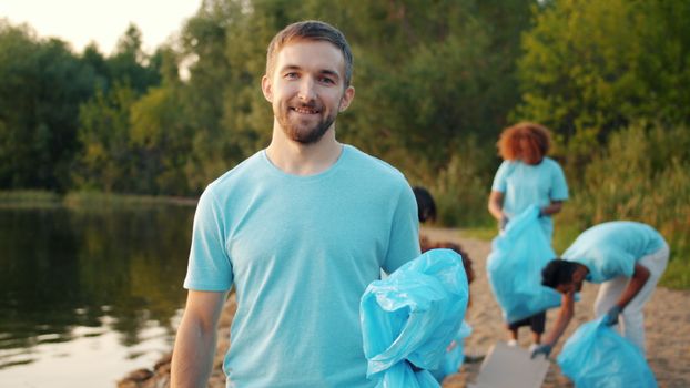 Group of volunteers cleaning riverside area by collecting trash, promoting environmental awareness.