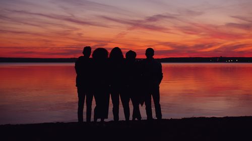Free Group of friends embracing while admiring a vivid sunset by the water. Stock Photo