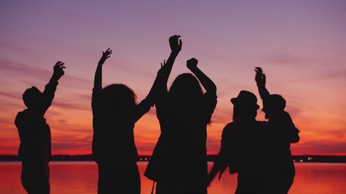 Free Silhouettes of people raising hands in celebration against a colorful sunset. Stock Photo