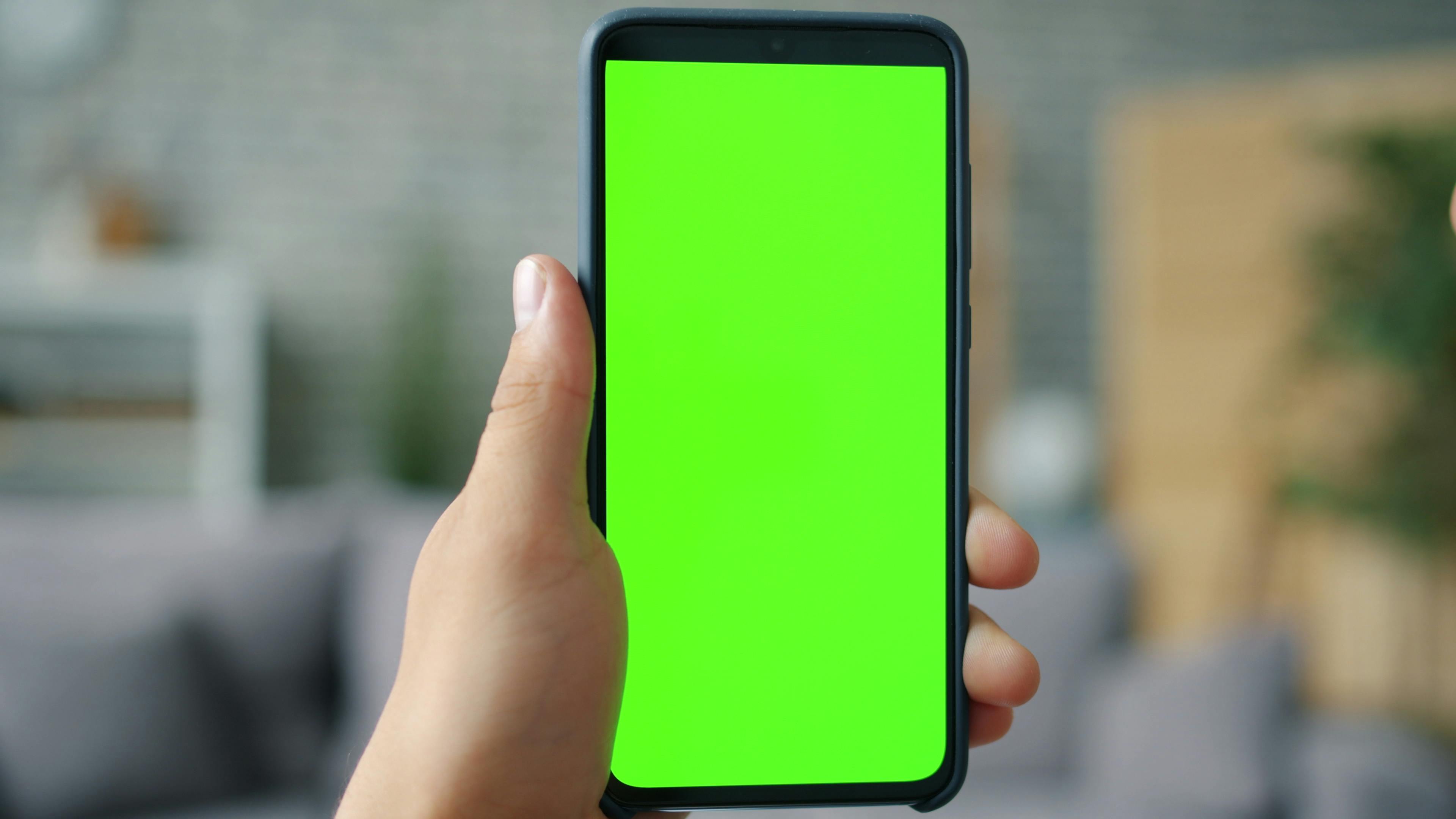 Close-up of hand holding smartphone with green screen, ideal for mockups.