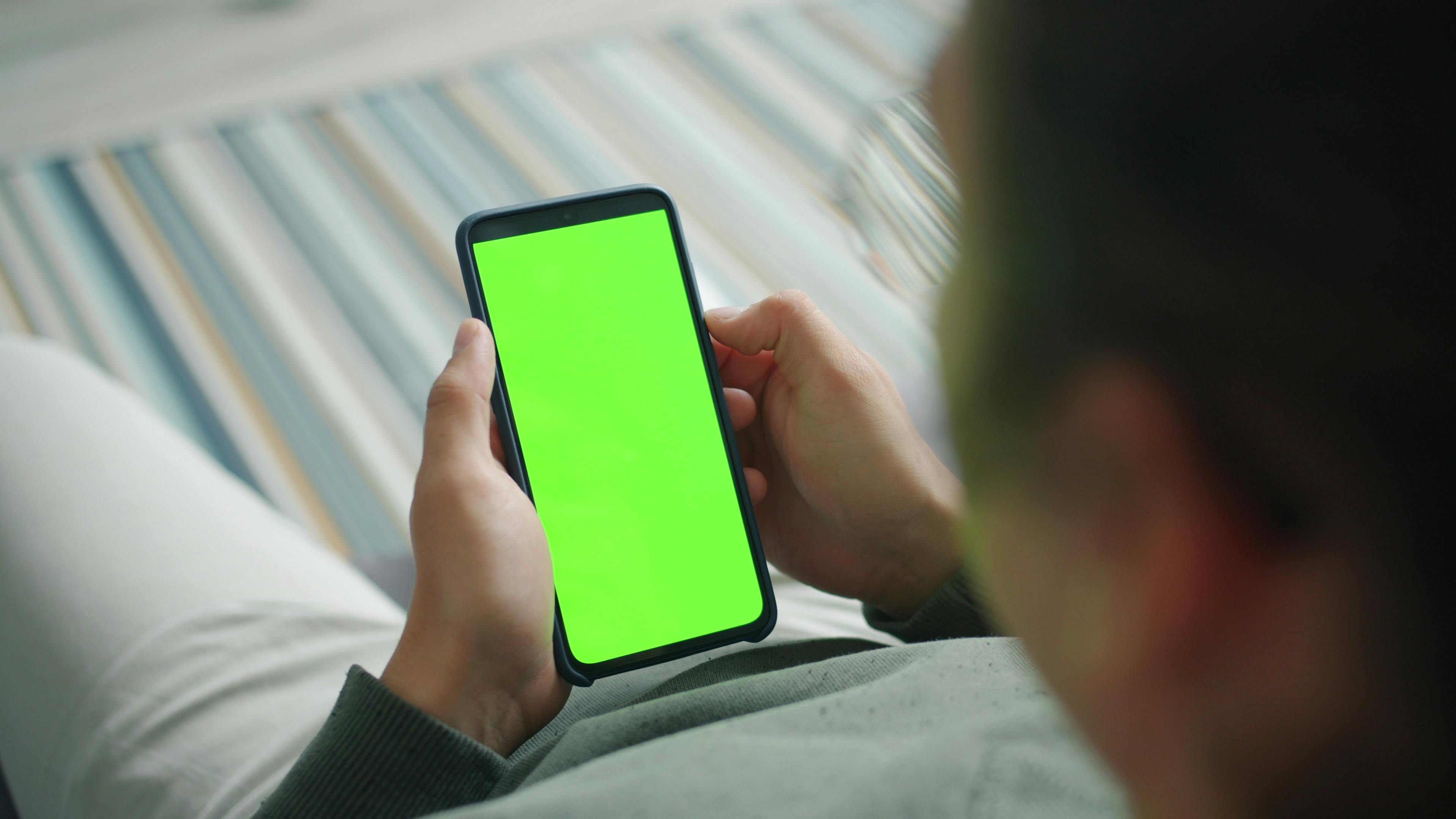 Close-up of person using phone with green screen for custom content display.