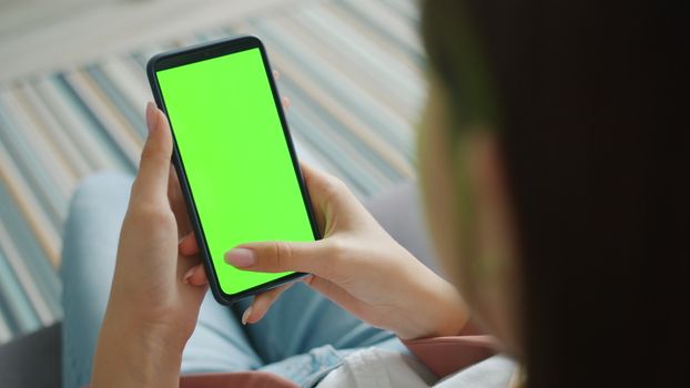 Close-up of woman holding smartphone indoors with green screen, perfect for apps or design showcase.