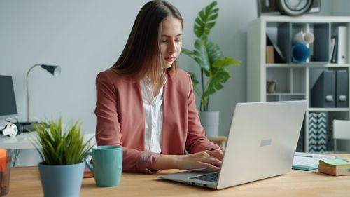 Free Confident young woman in business attire working on computer in modern office setting. Stock Photo